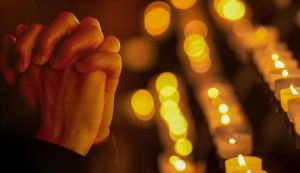 Praying hands with a background of lit candles.